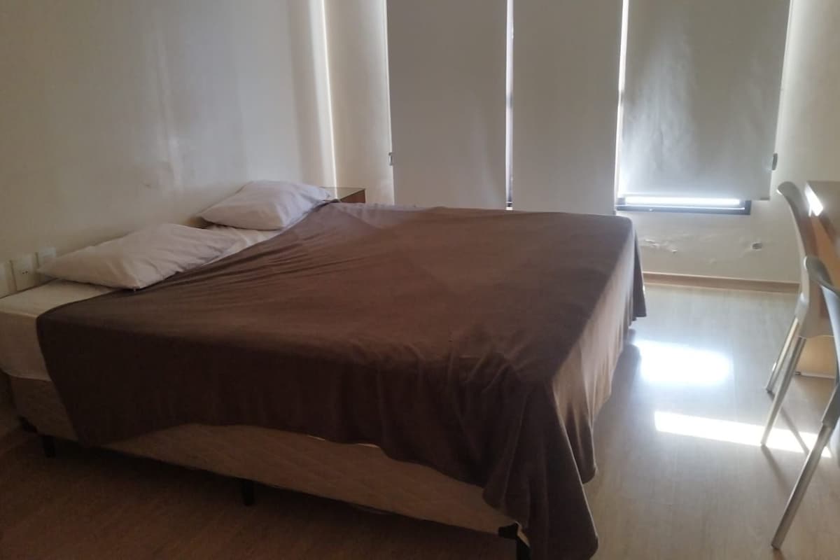 Un lit simple avec une couvre-lit marron, une table de chevet et une petite table à poser près du lit.