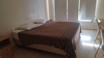 A single bed with a brown bedspread, a nightstand, and a window with blinds.