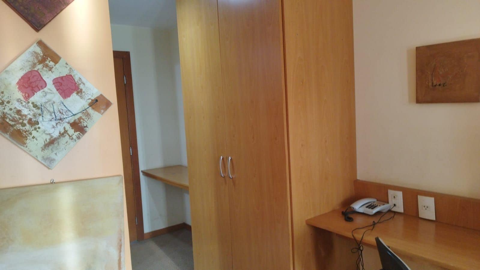 Une pièce comprenant une armoire en bois, un bureau avec un téléphone et une œuvre d’art accrochée au mur.