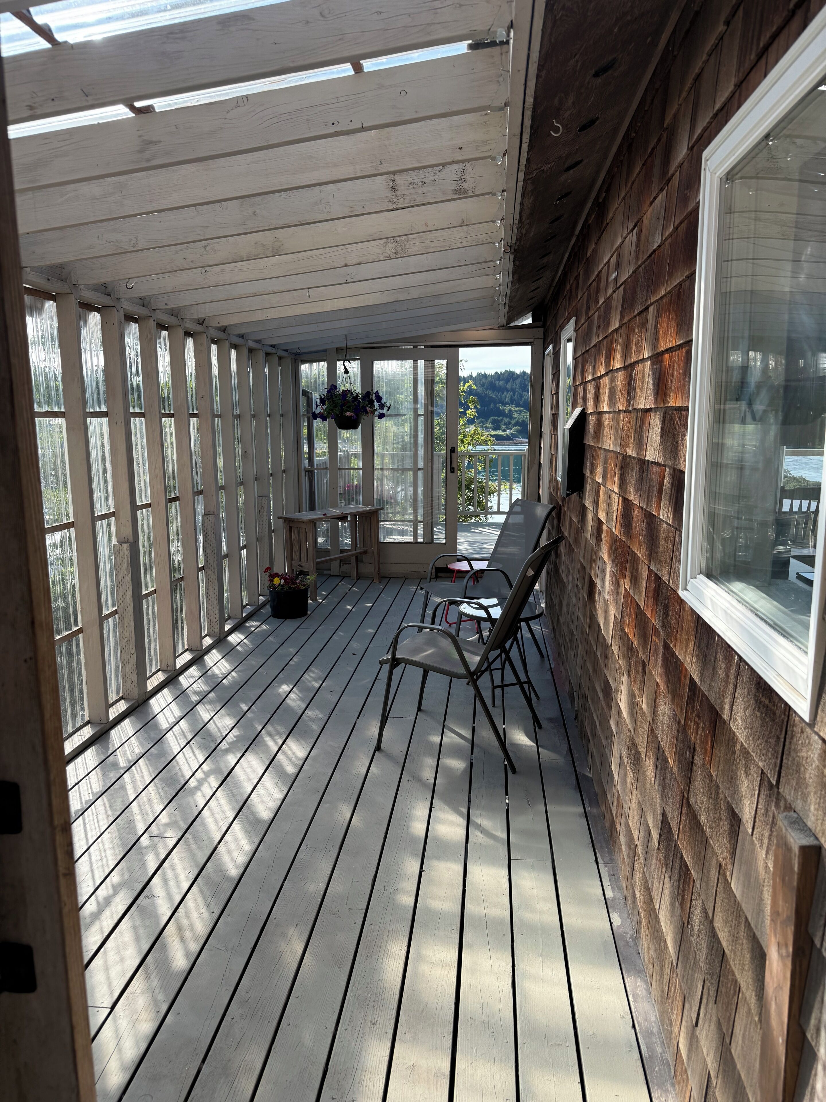 A covered porch with wooden railings, a table with chairs, and a view of a lake.