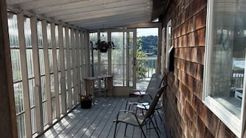 A covered porch with wooden railings, a table with chairs, and a view of a lake.