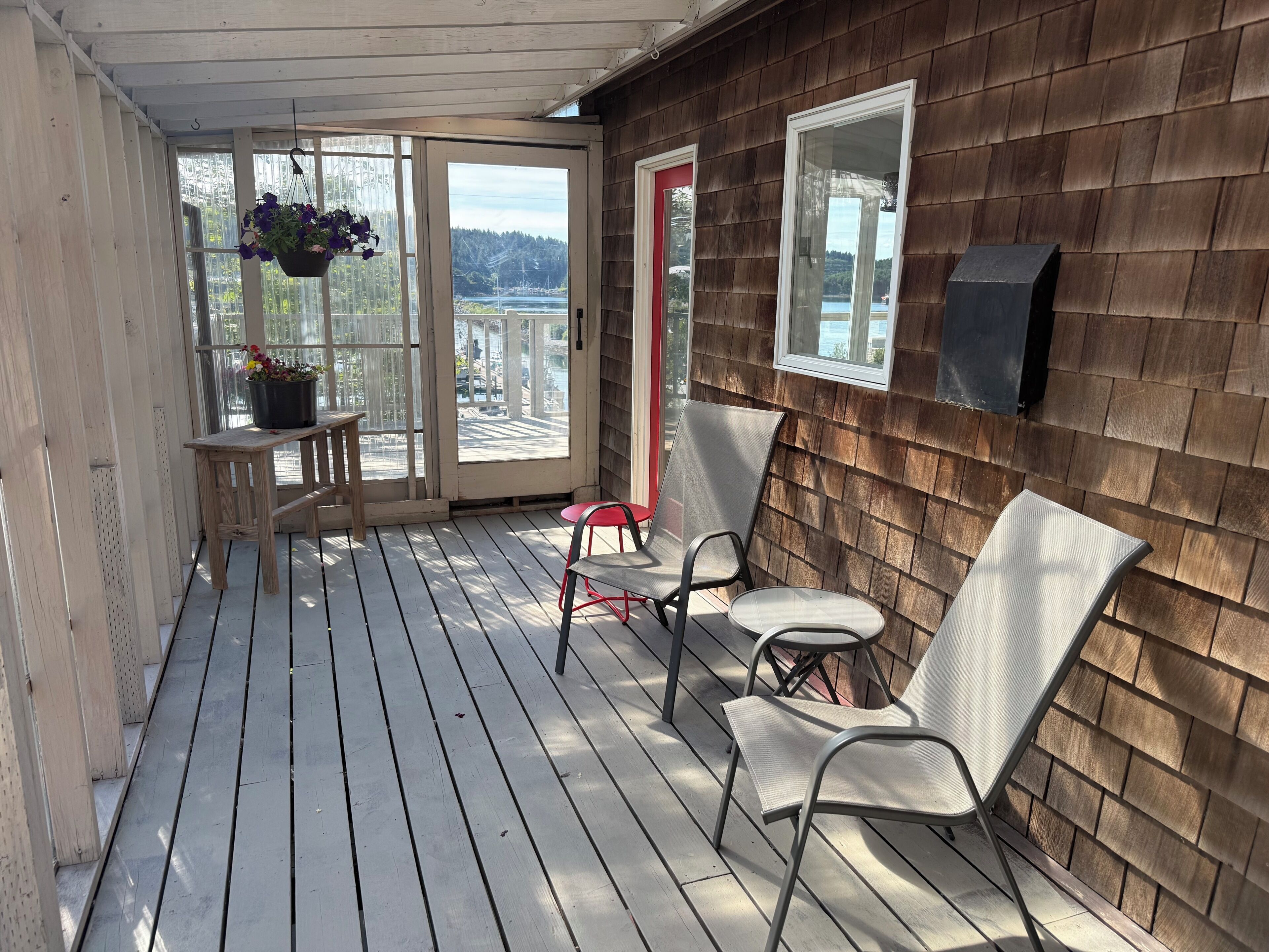 Une terrasse en bois avec une table et des chaises, une plante en pot et une porte rouge.