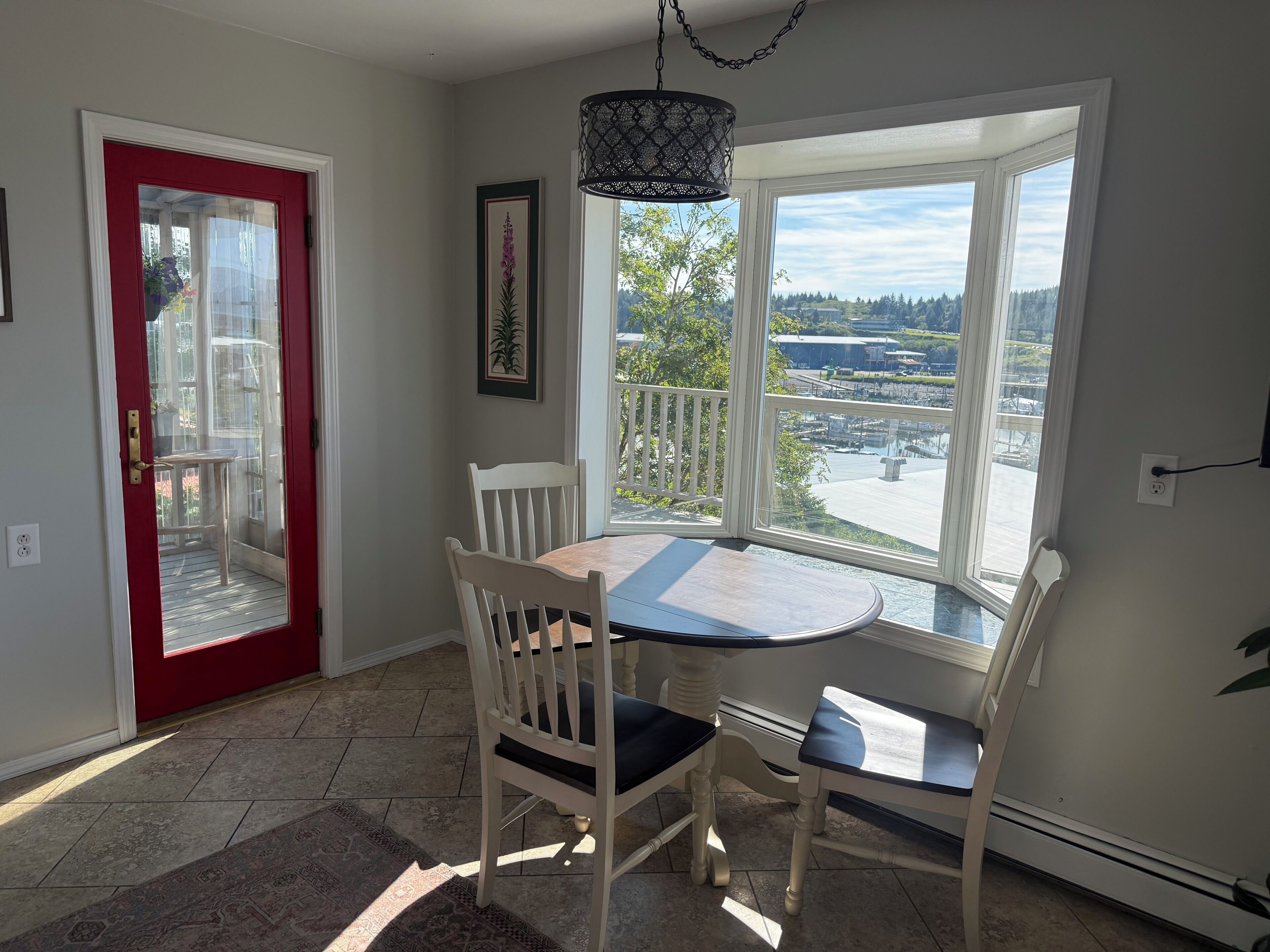 A dining area with a table and chairs, a red door, a window with a view, and a hanging light fixture.