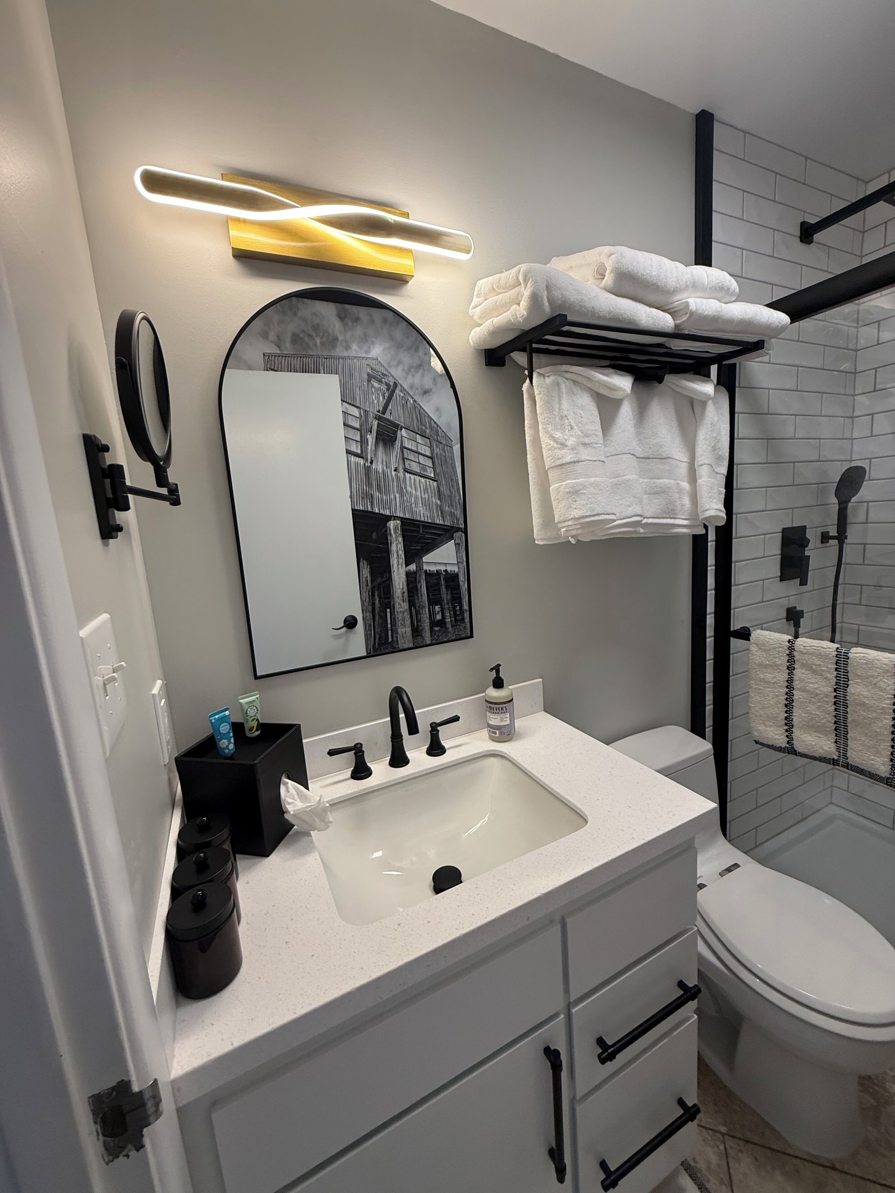A modern bathroom with a white sink, black faucets, a mirror, and a towel rack.