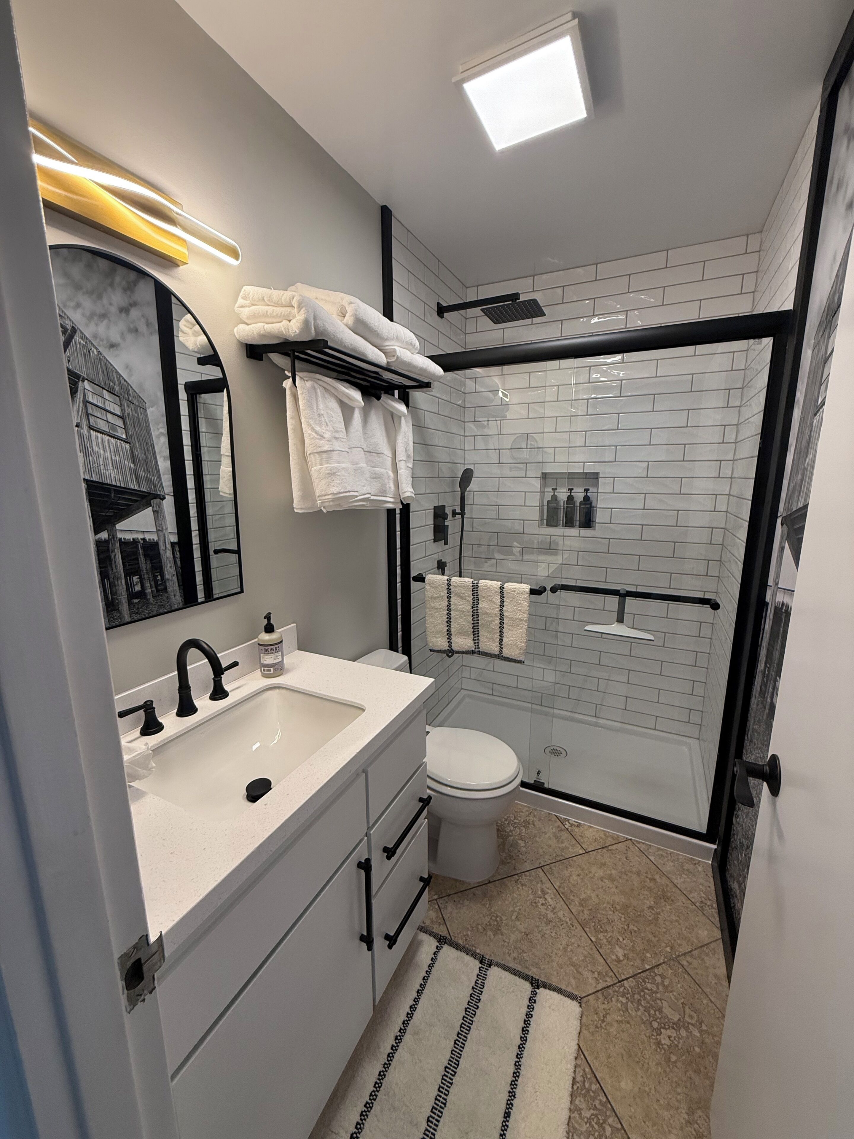 A modern bathroom with a white sink, black faucet, and a glass-enclosed shower area.