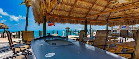 A beachside lounge with a thatched roof, wooden tables, and chairs, overlooking the ocean.