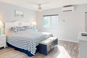 Ein Schlafzimmer mit einem Bett, Nachttischen, einer Bank, einem Deckenventilator, einem Fenster und einer Klimaanlage.