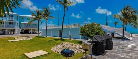 Una propiedad frente a la playa con piscina, zona de barbacoa y una escalera que lleva a un edificio con balcones.