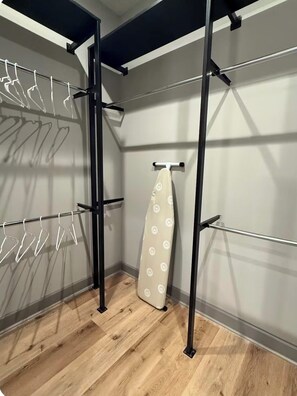 A corner of a room with a wooden floor, a metal rack with clothes, and a white ironing board. - Modern Peaceful Apartment in Downton Dallas - City Views - Parking - Balcony (Dallas)