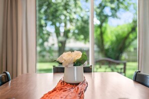 Une table à manger sur laquelle est posé un vase blanc contenant une seule fleur blanche, le tout placé sur un set de table en fibres tressées.