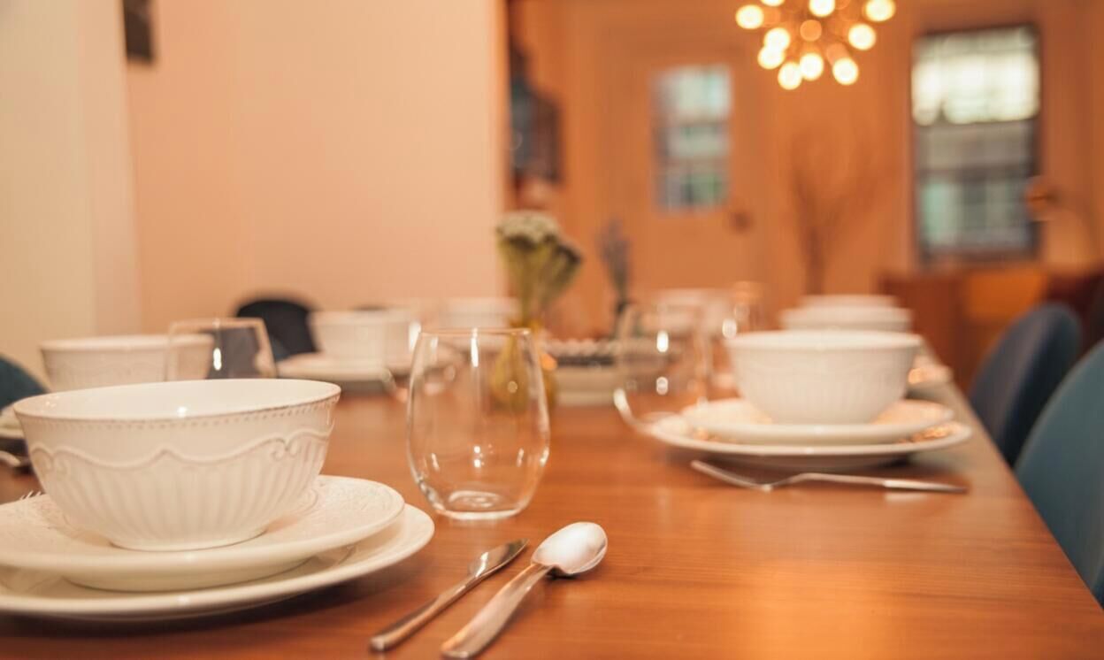 A dining table set with white bowls, plates, and cutlery, with chairs around it.