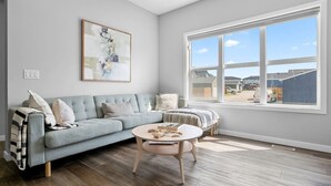 Ein Wohnzimmer mit einem hellblauen Sofa, einem runden Couchtisch und einem großen Fenster mit Blick auf eine Wohngegend.