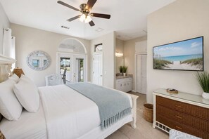 Una camera da letto con un letto, una ventola a soffitto, una televisione, una cassettiera e vista sulla spiaggia.