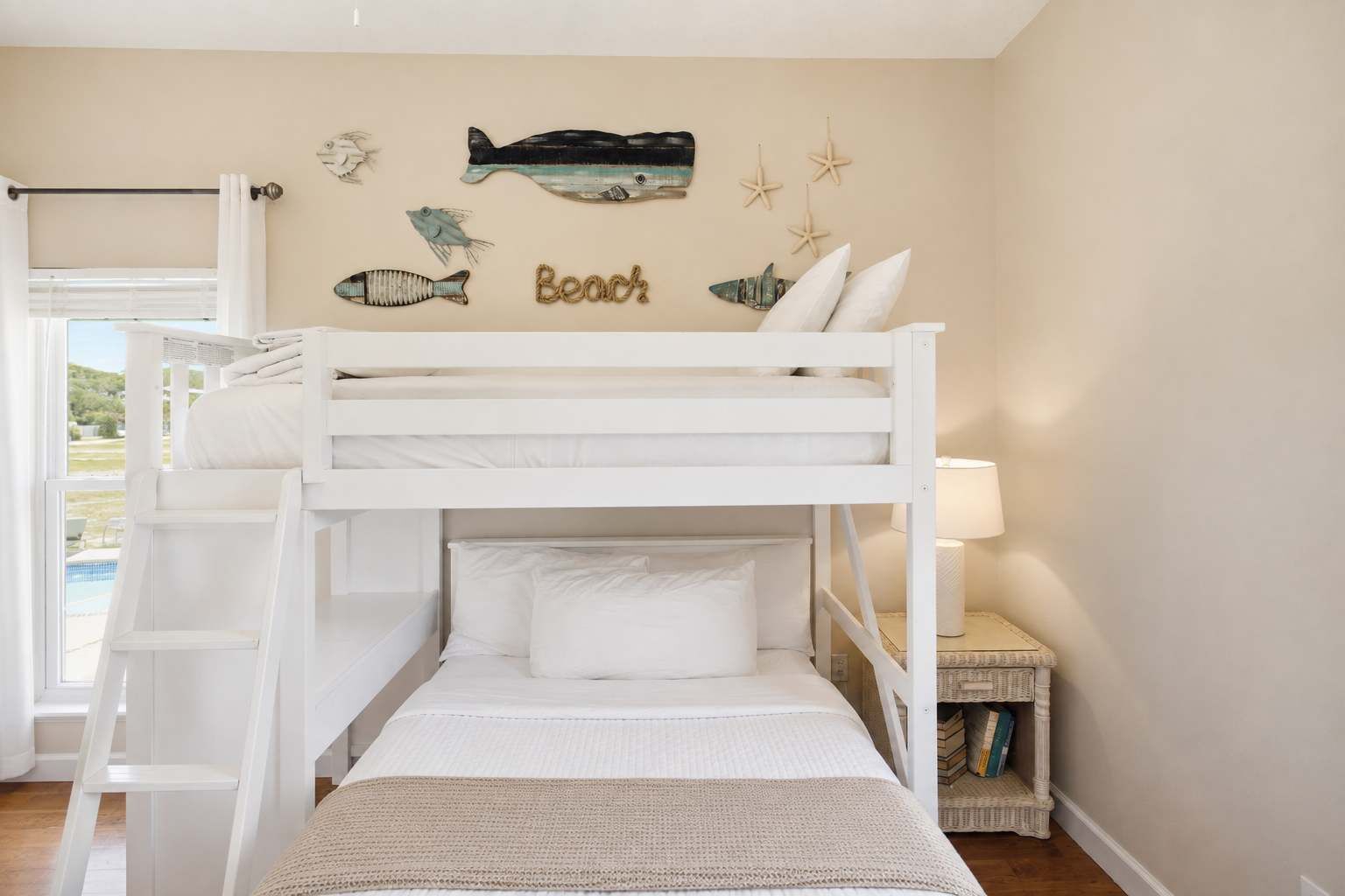 A bunk bed room with a view of a pool, a wall with fish and starfish decorations, and a lamp on a bedside table.
