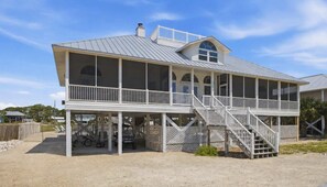 Een strandhuis met twee verdiepingen, een overdekte veranda, een trap en een omheinde tuin.