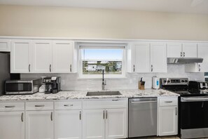 A modern kitchen with white cabinets, a built-in microwave, coffee maker, toaster, and dishwasher. - Perfect SGI Paradise- 5 Bedroom+ POOL SGI (Saint George Island)