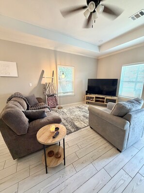 A modern living room with two sofas, a TV, and a ceiling fan.