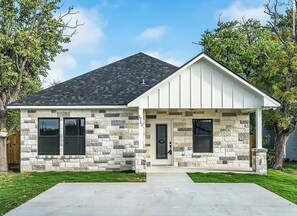 A two-story house with a stone facade, a front porch, and a driveway.