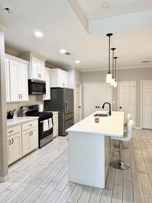 A modern kitchen with white cabinetry, stainless steel appliances, and a central island with a sink.