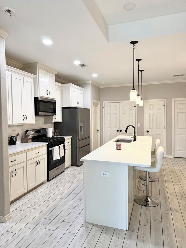 A modern kitchen with white cabinetry, stainless steel appliances, and a central island with a sink.