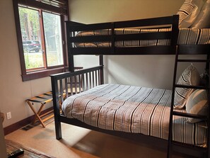 Een stapelbed met een gestreept matras, een houten trap en een raam met uitzicht op een geparkeerde auto.