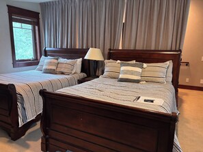 Een slaapkamer met twee houten bedden, strepenbeddengoed en een raam met gordijnen.