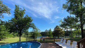A wooden deck with a swimming pool, surrounded by trees and a view of a lake.