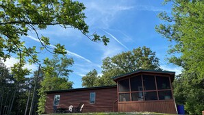 A cabin with a large windowed porch, surrounded by trees and a clear sky.