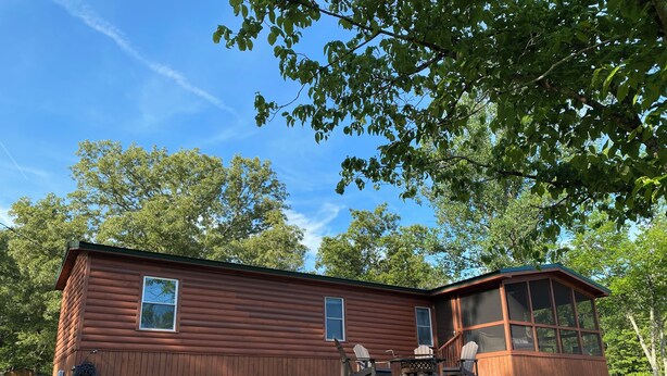 A wooden cabin with a large windowed porch, a dining table, and chairs.
