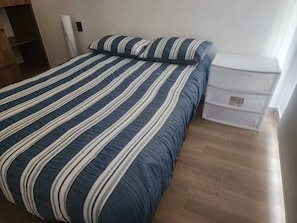 Un lit avec une literie à rayures, une table de chevet blanche et un meuble de rangement.