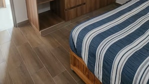 Makuuhuoneessa on puinen vaatekaappi, raidallinen vuodevaatteilla varustettu sänky ja laatoitettu lattia.