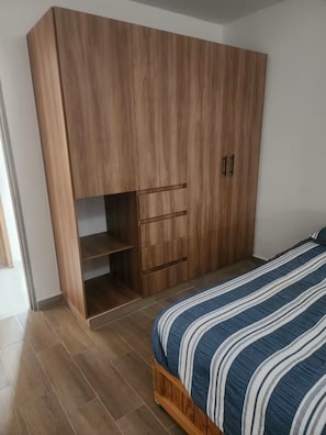 Une chambre avec une armoire en bois, un lit avec une literie à rayures et un sol carrelé.