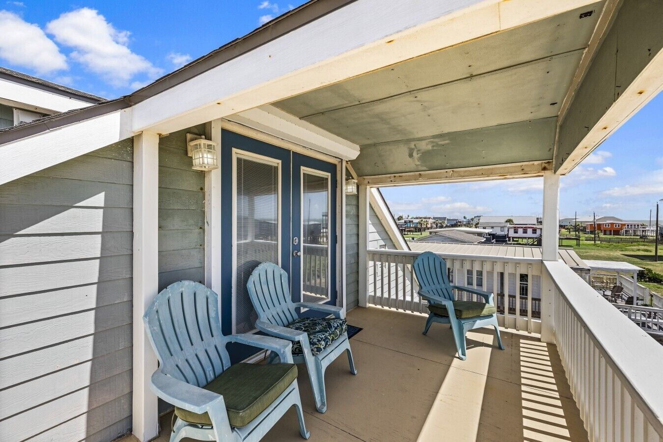 A covered balcony with two Adirondack chairs and a small table, overlooking a residential area.