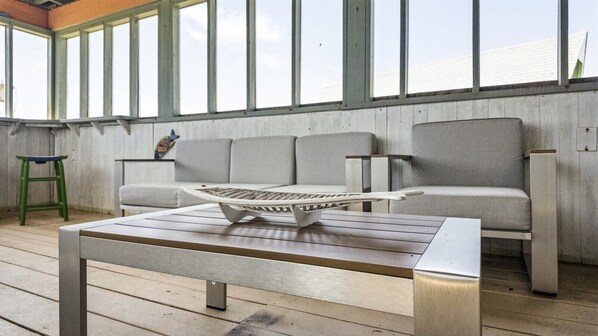 A conservatory with a wooden floor, a grey sofa, and a metal table with a tray.