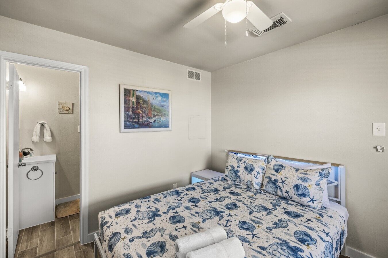 A bedroom with a bed, a painting on the wall, and a ceiling fan.