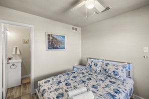 A bedroom with a bed, a painting on the wall, and a ceiling fan.