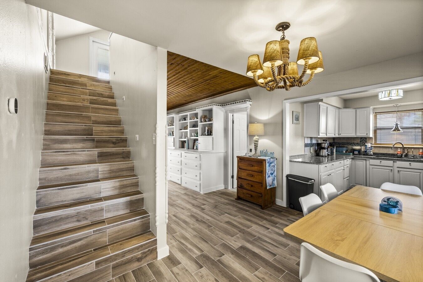A modern kitchen with white cabinets, a wooden dining table, and a chandelier.