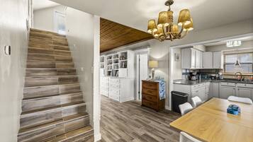 A modern kitchen with white cabinets, a wooden dining table, and a chandelier.