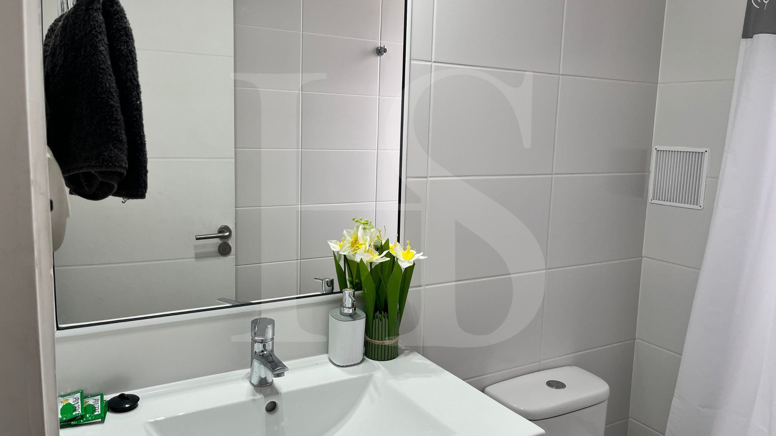 Ein Badezimmer mit weißem Waschbecken, Spiegel, Toilette und Duschvorhang.