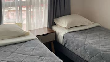 Una habitación de hotel con dos camas, una mesita de noche y una ventana con cortinas.