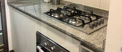 Une cuisine équipée d’une cuisinière à gaz, d’un four et d’un plan de travail en granit.