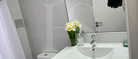 A bathroom with a white sink, a mirror, and a toilet. There is a bouquet of flowers on the sink.