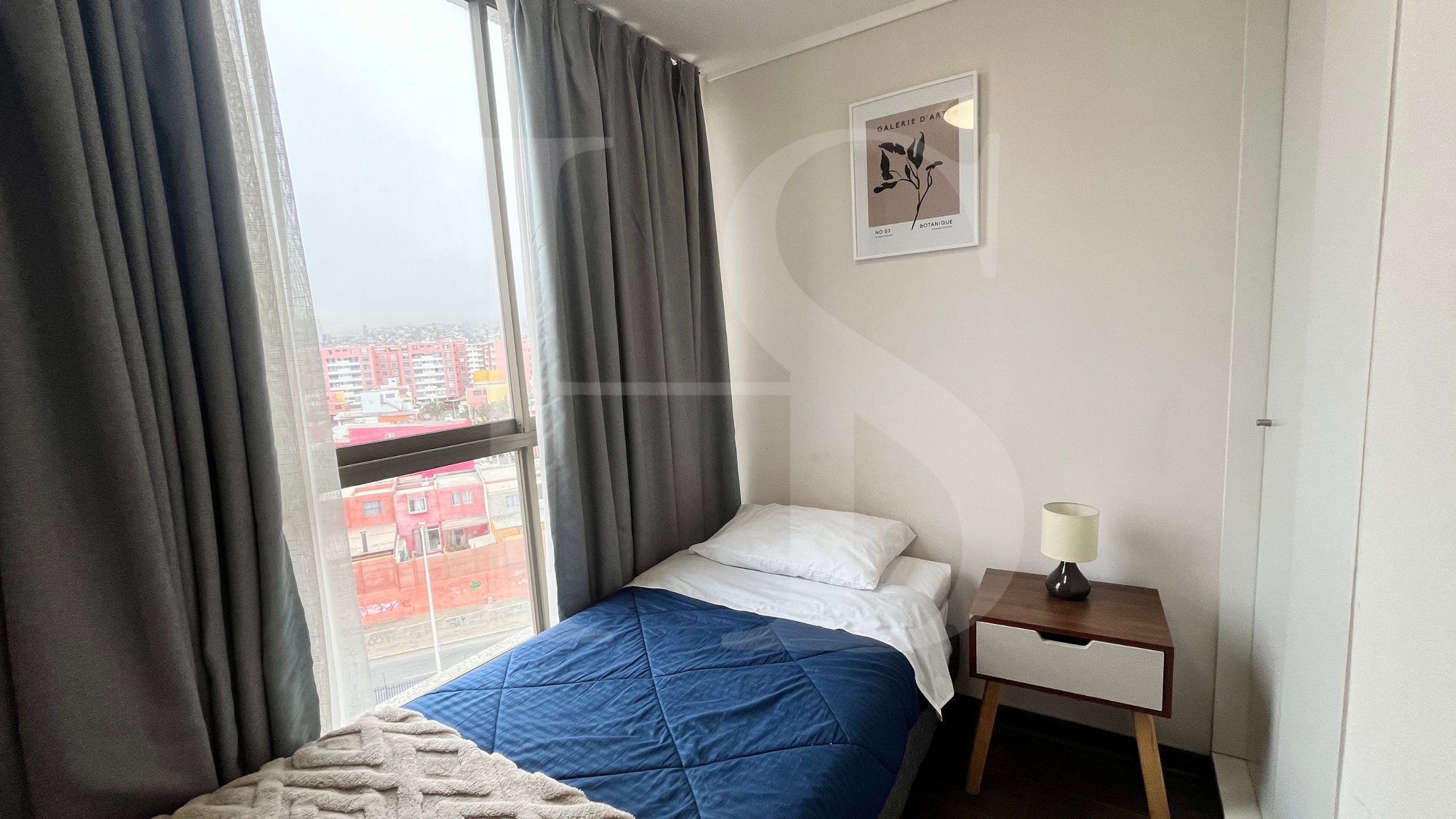 Quarto de hotel com cama, mesa de cabeceira, luminária e janela com cortinas.