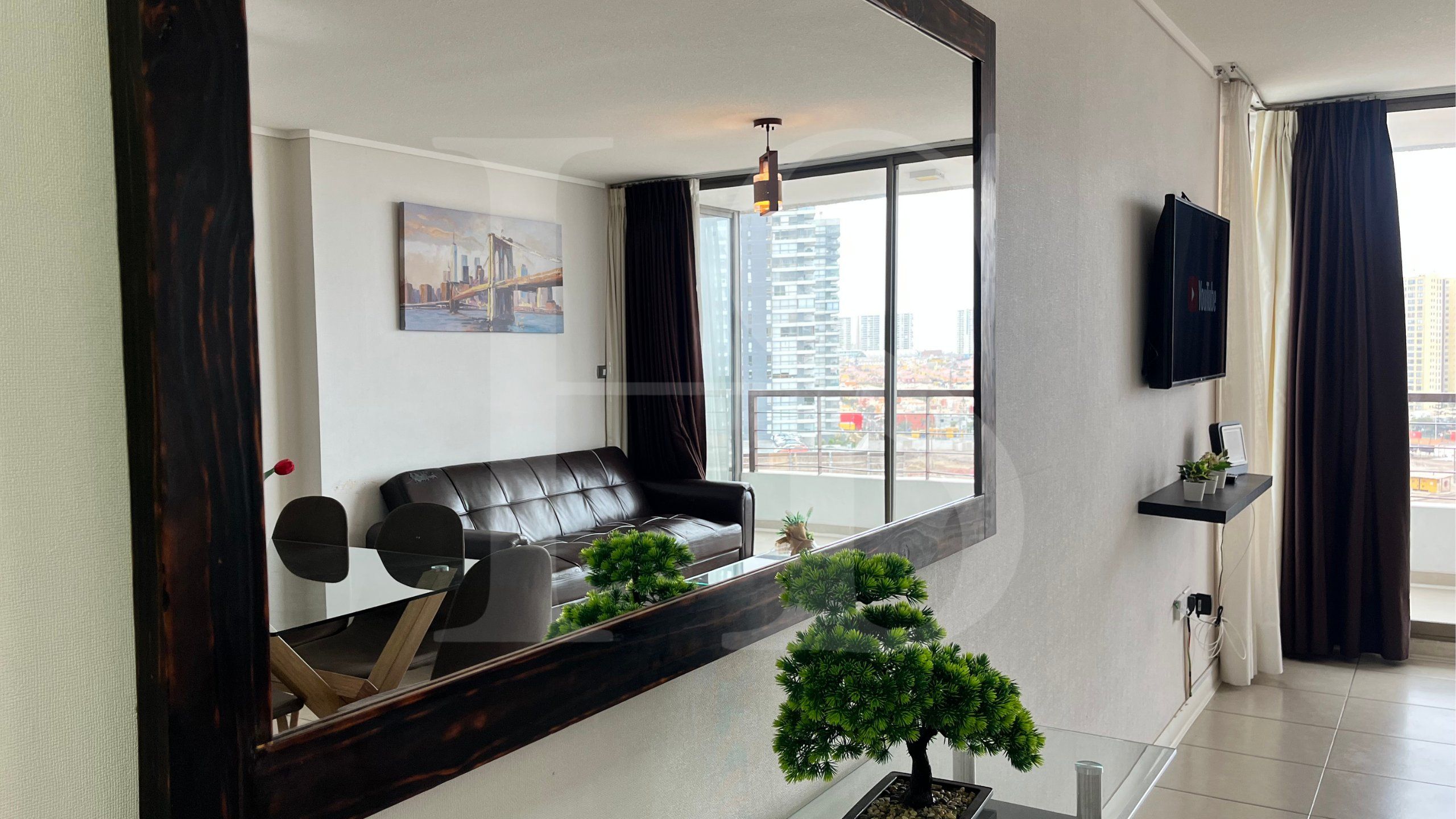 A modern living room with a leather sofa, a glass coffee table, and a cityscape view through large windows.