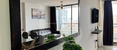 Un salon moderne avec un canapé en cuir, une table basse en verre et une vue sur le paysage urbain grâce à de grandes fenêtres.