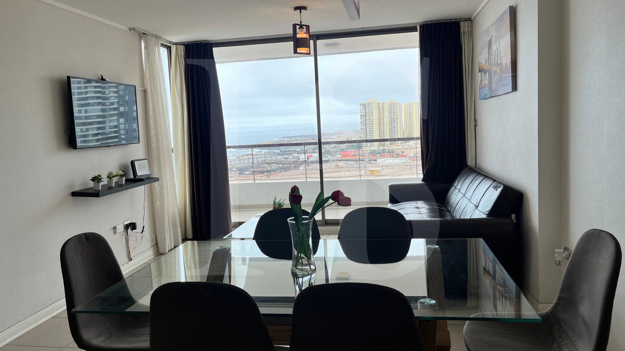 Uma área de jantar moderna com mesa de vidro, cadeiras pretas, um sofá e vista para o horizonte urbano através de grandes janelas.