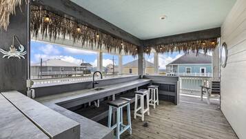 Ein überdachter Außenbereich mit Bar, einer Betonplatte, Barhocker und Blick aufs Meer.