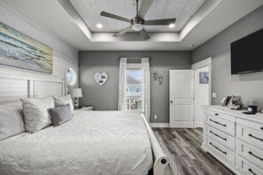 Ein Schlafzimmer mit einem Bett, einer Kommode, einem Deckenventilator, einem Fenster und einem an der Wand befestigten Fernseher.