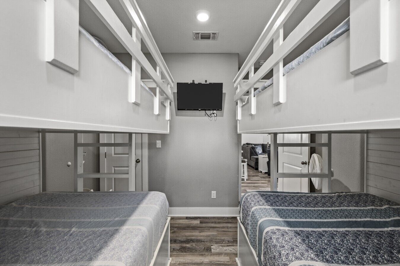 A room with bunk beds, a flat-screen TV mounted on the wall, and a wooden floor.