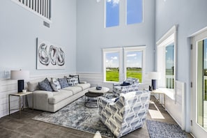 A spacious living room with a sofa, armchairs, and a coffee table. There are large windows providing a view of the outdoors. - Regal Gal | Bird Watcher`s Coastal Escape (Galveston)